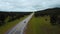 Drone flying low over traffic on highway road between wild clean green forest hills with trees on cloudy summer day.