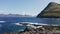 Drone flying over rock beach, man sitting in front of landscape. Young man resting and looking rough blue sea, green