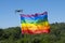 Drone flying with a rainbow flag attached to it on the outdoors with clear blue sky. Lgtbiq concept