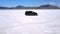 Drone flying sideways following silver minivan car driving in the middle of breathtaking Bonneville salt lake desert.