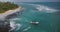 Drone flyover shot of exotic resort beach with little boat, tropical trees, foamy waves crashing over beautiful shore.