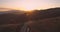 Drone following lonely car driving on curved mountain road reflecting the sunset lights