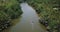 Drone following, tilt down on small white boat sailing along beautiful jungle river in wilderness with sun reflections.