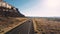 Drone follows car driving along highway road between epic steep canyon mountain ridge and amazing desert skyline in USA.