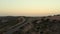 Drone footage of a biker on a route going through the sand dunes with grassy plants at sunset