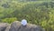 Drone footage of a freelancer working on a laptop in the open air sitting on the edge of a rock mountain over a