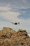 A drone hovering with rocks, clouds and blue sky in the background