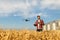 Drone hovers in front of farmer with remote controller in hands near grain elevator. Quadcopter flies near pilot