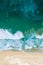 Drone looking down over deep blue and green waves crashing to shore as people walk along the beach