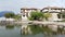 Drone moving backward - old little village and boats reflected on Lake como coastline