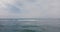 Drone moving up and forward above waves reaching shore to reveal amazing open ocean panorama and epic cloudy skyline.