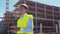 Drone operator holding remote controller. Professional builder in helmet and vest standing in front of construction site