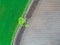 Drone photo of a fresh bright green wheat field separated from a recently plown field by the road. There is a tree by