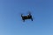 A drone, a quadrocopter with a camera for video shooting, flies against a blue sky