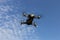 A drone, a quadrocopter with a camera for video shooting, flies against a blue sky with clouds