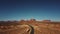 Drone rising up above empty desert road to reveal amazing endless wide open spaces of sunny Monuments Valley in USA.