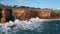Drone rugged coastal rocks washing by ocean waves. Sea water breaking on cliffs.