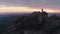 Drone shot of lonely man standing on top of a mountain and enjoying the sunset