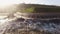 Drone shot people running from big waves covering them near sea wall on wonderful sunny day slow motion