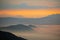 Drone shot of silhouettes of green-covered hills in mist at sunset, cool for background