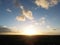 Drone shot of the sunrise over a wide grass field with green trees under blue sky