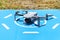 The drone is standing on a blue landing field on grass, the plastic propellers are turned off and the camera on the gimbal is visi