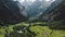 Drone tilts up from alpine mountain meadows and chalet houses to reveal epic snowy peaks ridge in Switzerland Alps.