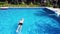 Drone tracking shot over a man swimming in a blue pool in a resort on summer day