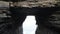 Drone traveling through the arch of a cliff to the seascape under the cloudy sky