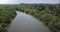 Drone turning left, following small white safari boat sailing along beautiful rainforest river in jungle wilderness.
