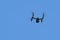 Drone with a video camera flies in the blue cloudless sky. Videofilming and videosurveillance from above. Copy space