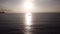 Drone view of glittering sun rising up over ocean horizon, reflecting sunlight on sea surface with boat floating.