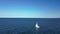 Drone view of small sailboat sailing on the horizon with blue sky background