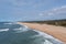 Drone view of a wide empty and endless golden sand beach with high sand dunes and vegetation behind