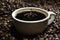 Drop of coffee falling into coffee cup sitting in a pile of freshly roasted coffee beans