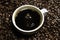 Drop of coffee falling into coffee cup sitting in a pile of freshly roasted coffee beans. Top view