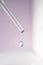 A drop of cosmetic oil falls from the pipette on a purple floral background.
