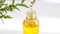 A drop of yellow essential or organic oil in a glass pipette above the bottle