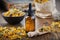 Dropper bottle of calendula essential oil, infusion or serum, healthy marigold flowers in bowl and paper bag of dry calendula.