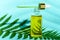 Dropper glass bottle with pipette and yellow cosmetic oil on blue background and fern leaf