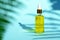 Dropper glass bottle with yellow cosmetic oil on blue background and leaf shadow