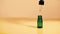 Dropper green glass bottle. Oily drops fall from cosmetic pipette on yellow background.