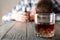 Drunk man holds bottle on wooden table with glass of whiskey