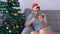 Drunken man near Christmas tree sitting on couch pays online using a smartphone.