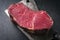 Dry aged raw Angus Sirloin Steak offered on a kitchen cleaver on a black board