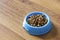 Dry cat food in blue bowl on wood laminate floor.