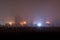 Dry dark grass field in front of foggy night depressive suburbs ghetto with