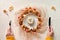 Dry floral wreath on plate with white pumpkin. Hands with fork and knife. Symmetrical central composition. Flat lay, top