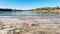 Dry grass is covered with hoarfrost. Lake shore with thawed water and ice patches on a frosty spring day. Sunny day with clear sky