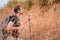 Dry grass flowers with blurred background of caucasian man hiker having fun walking up mountain on trail with dry grass field in